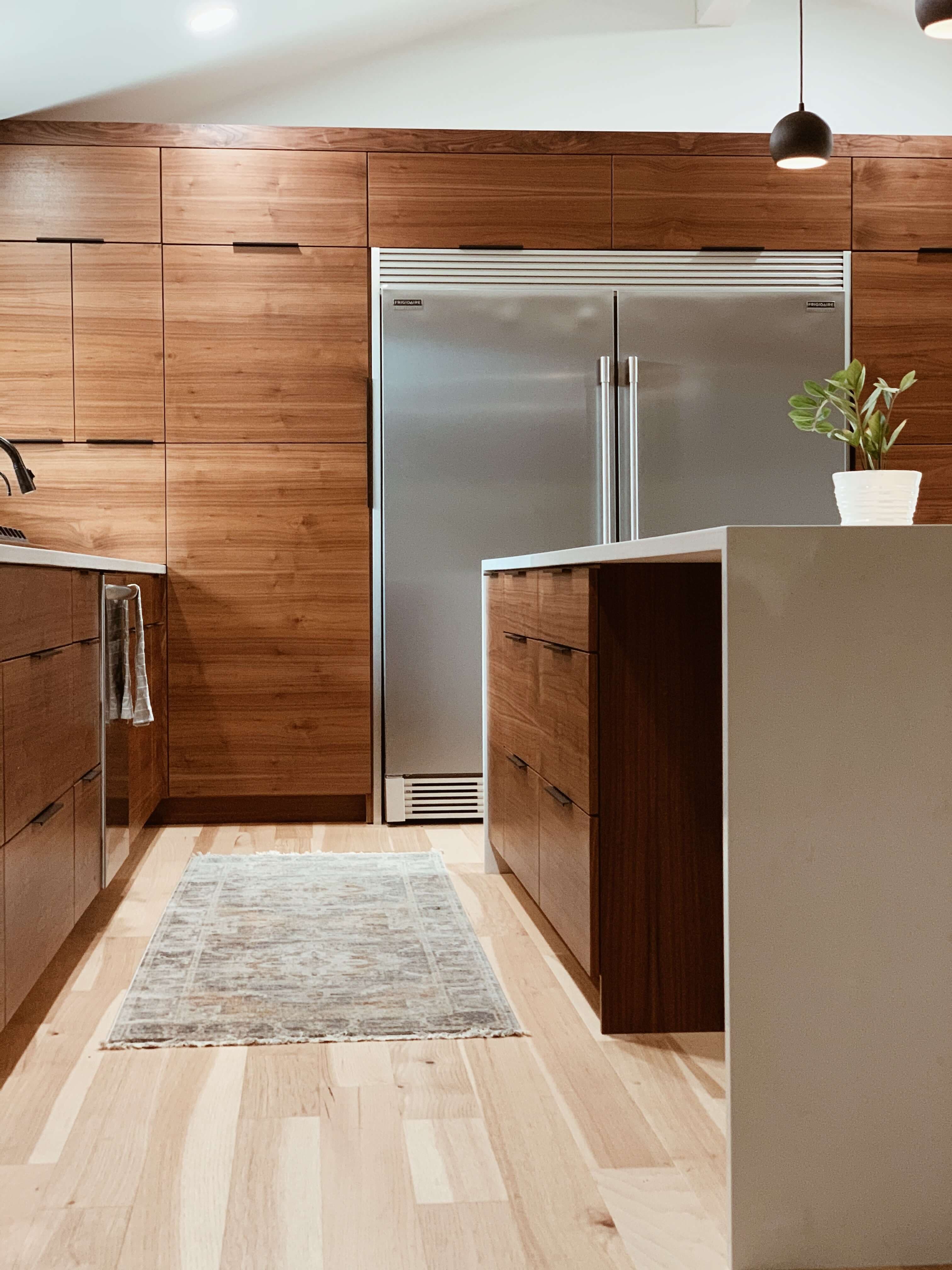 PAS wooden veneered kitchen picture. Table top, with plant and fridge. White wall and lighting.